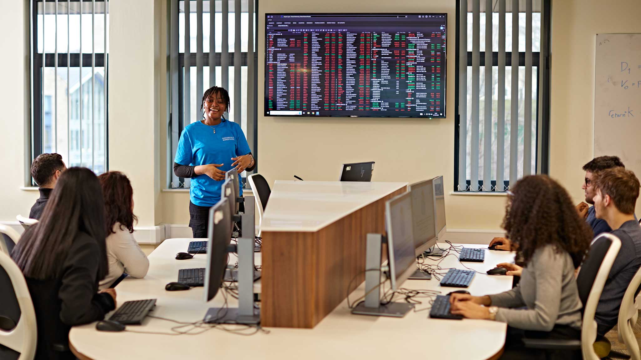A student ambassador speaks to a crowd of prospective students who are sat in Huddersfields trading room