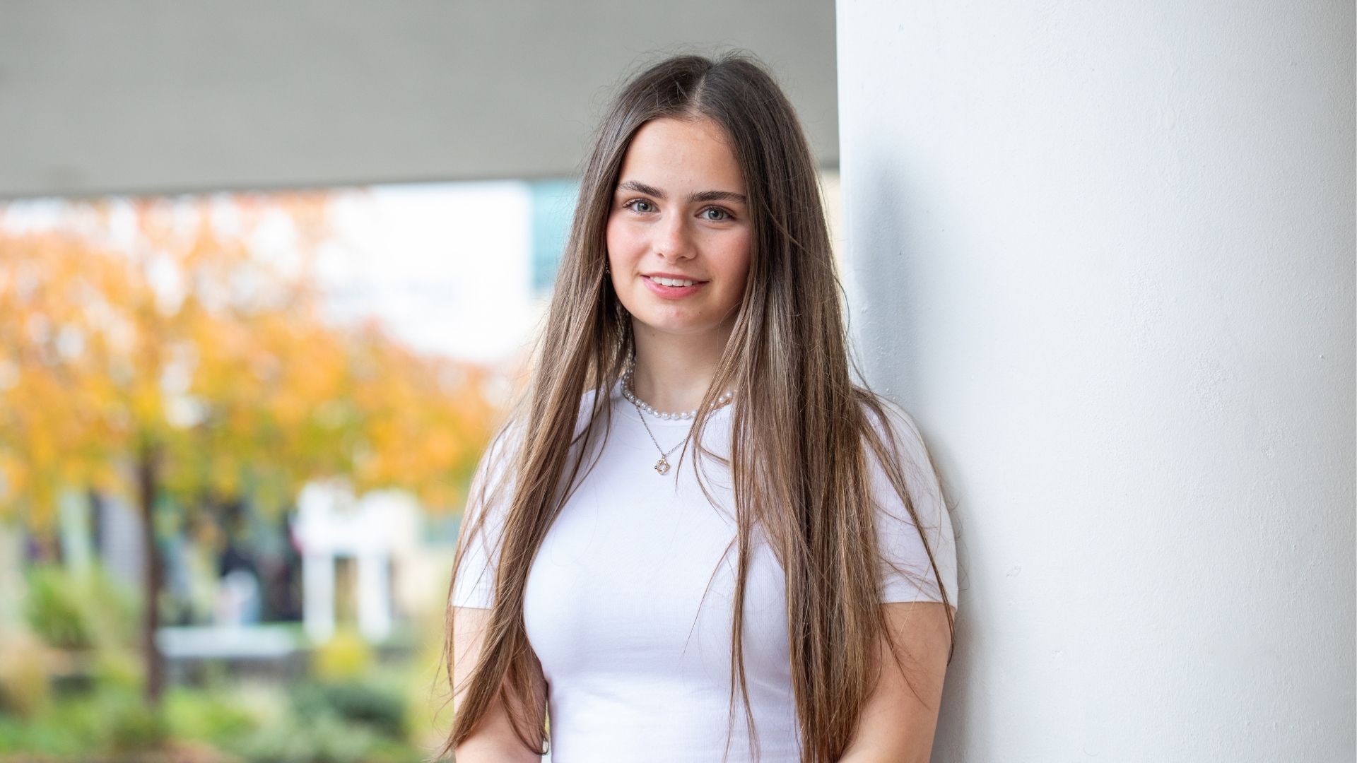 A smiling student leaning against a white wall