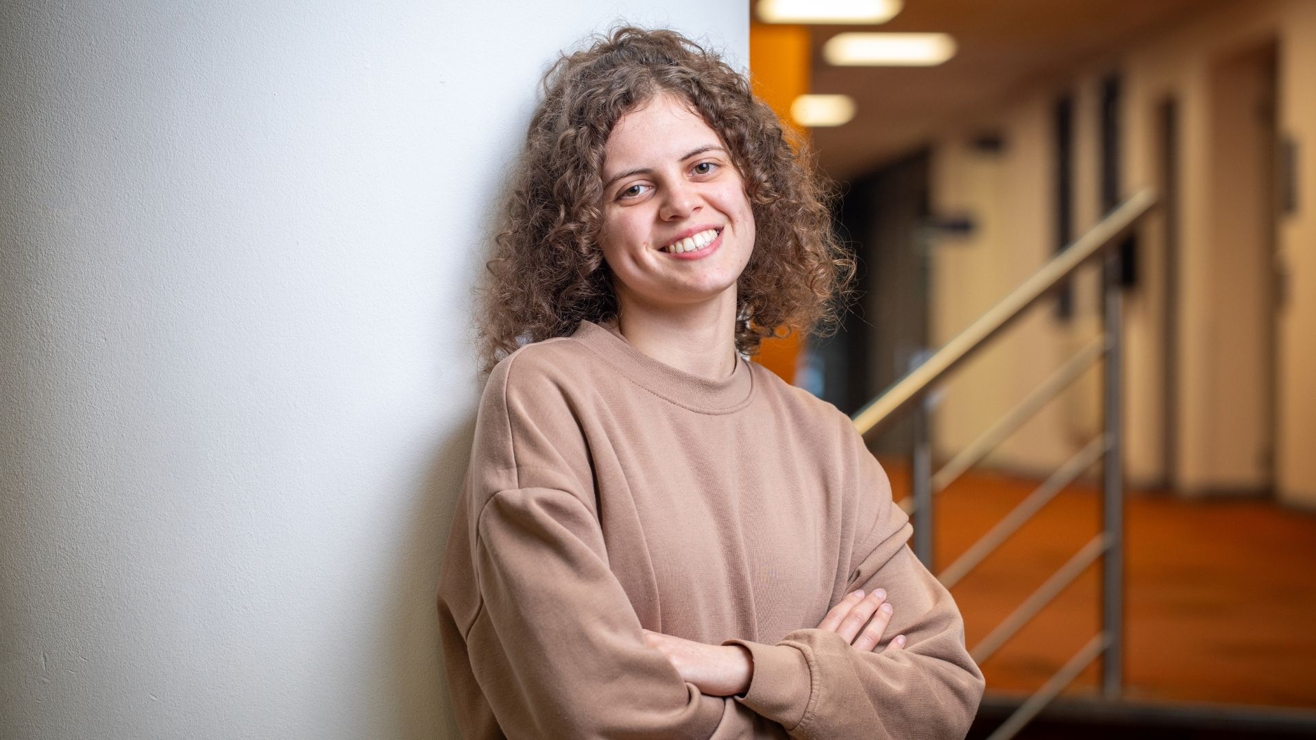 A student leaning against a wall smiling