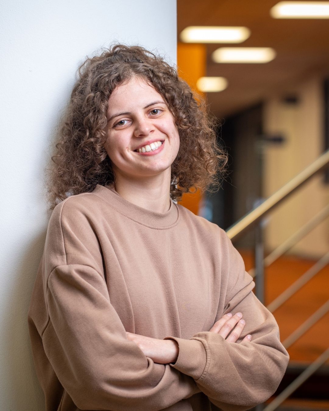 A student leaning against a wall, arms folded, smiling