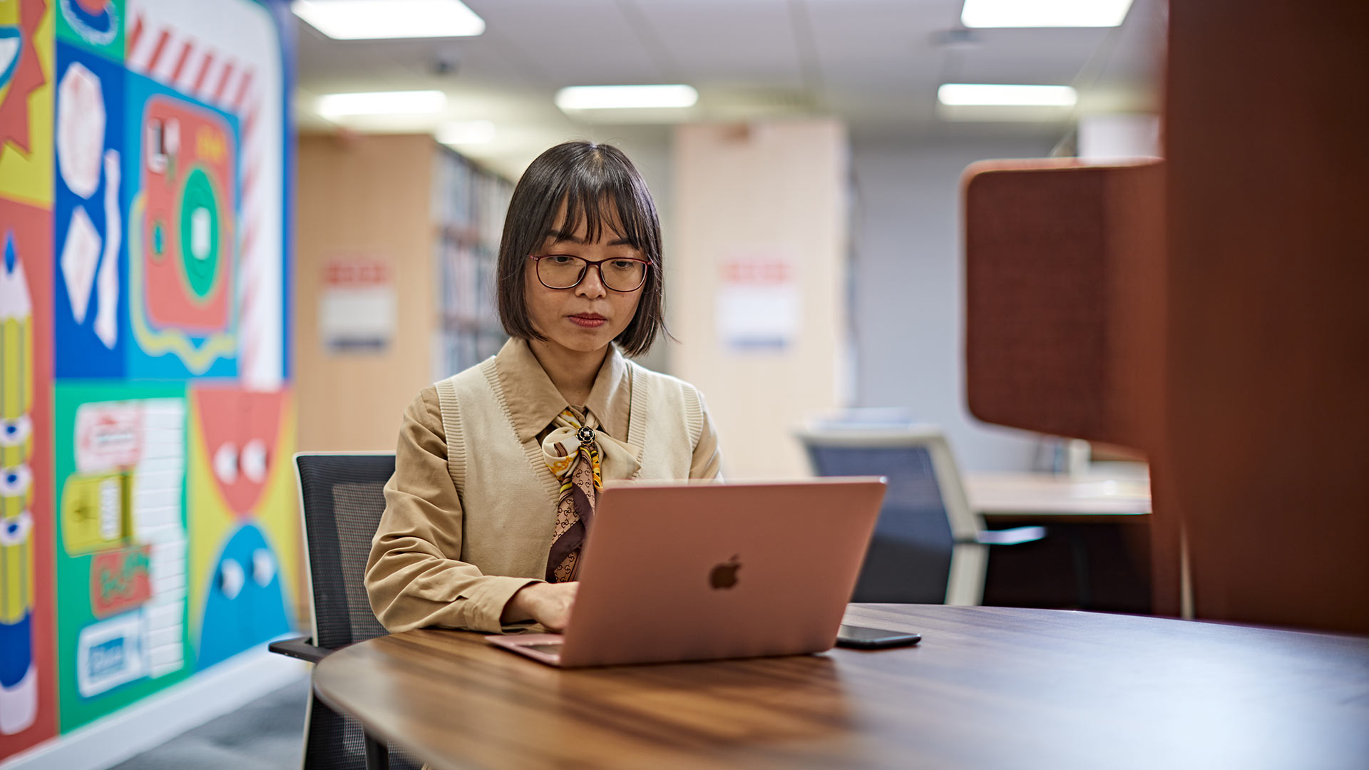 A student studying in a library, using a laptop device.