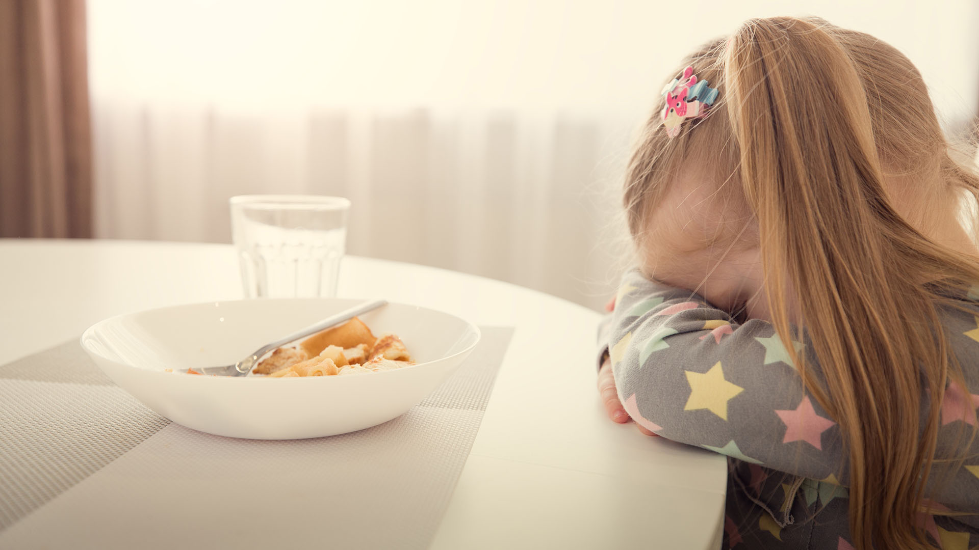 Young girl sat at the dining table with her head in her hands upset