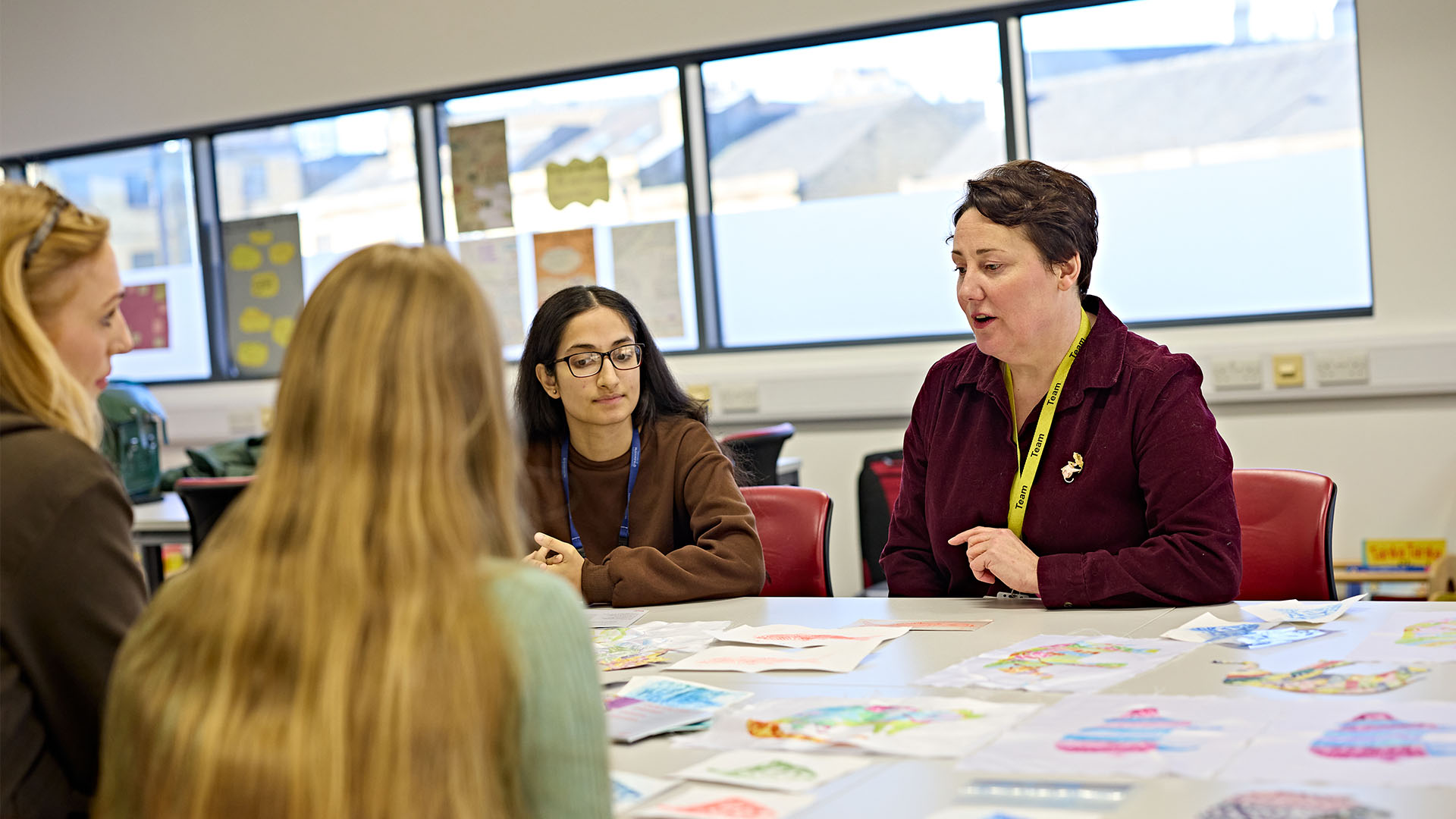 Teacher sat with three students on a table, discussing the art pieces on the table