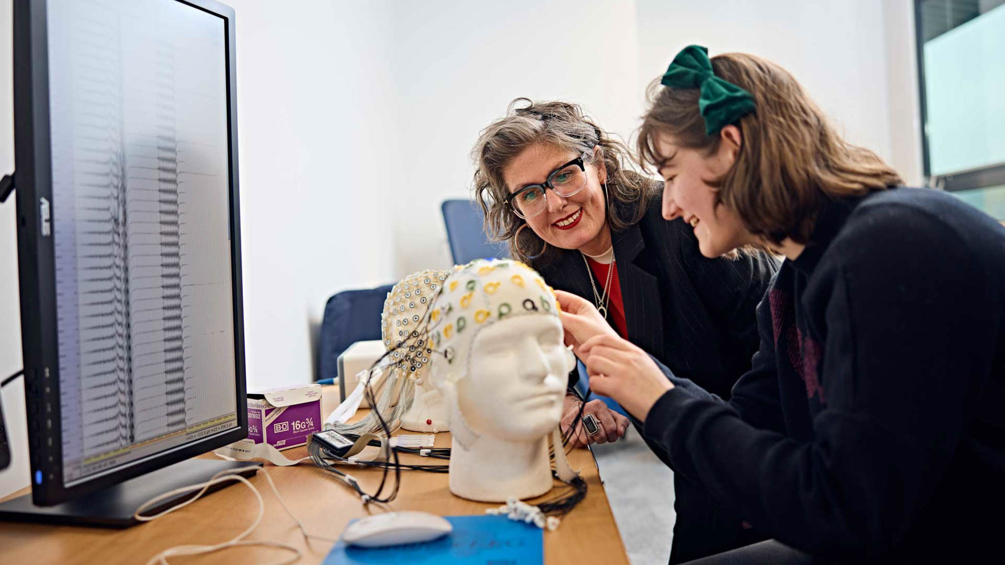 A psychology student and lecturer testing the measurements of an electroencephalography (EEG) cap before using it to measure electrical activity in the brain of a participant in their experiment.